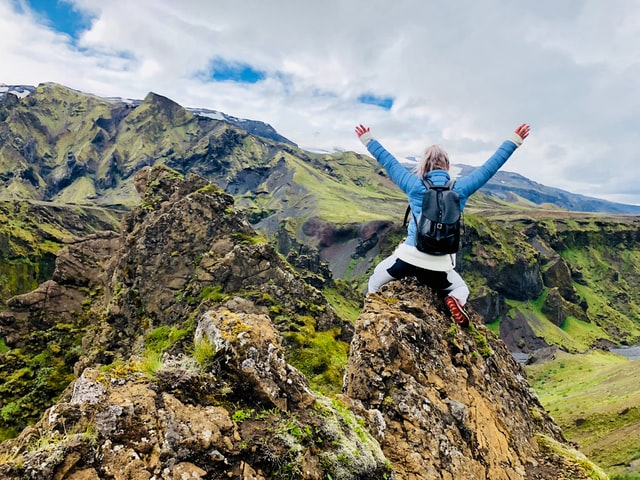 person victoriously sitting on the summit of a mountain